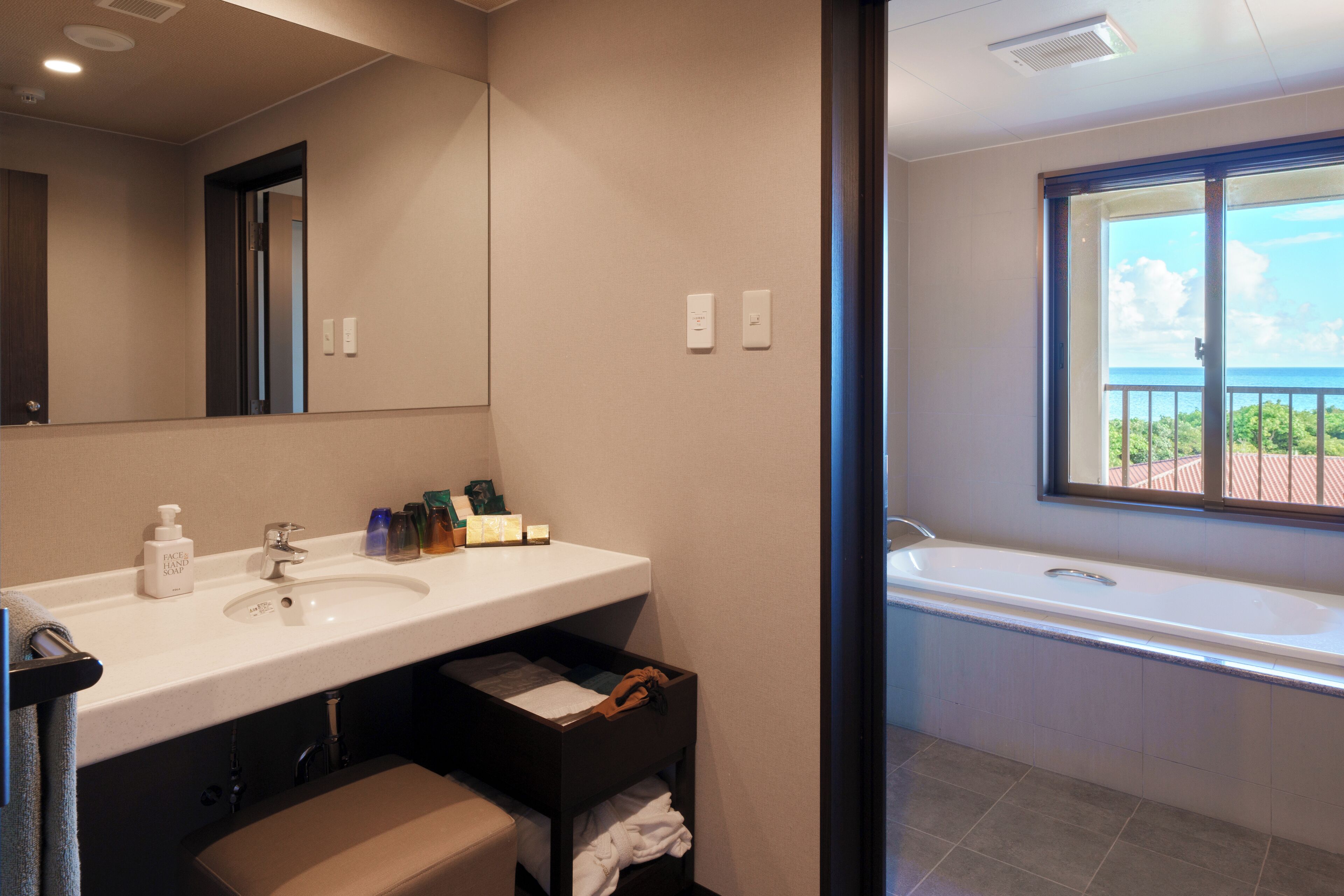 A modern bathroom with a large mirror, a sink, a bathtub, and a window offering a view of the outdoors.