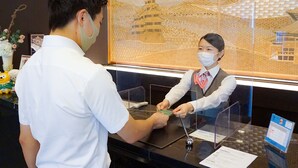 A reception desk with a glass partition, a framed artwork of a pagoda, and a small table with a calendar and a phone. - Hotel Route-Inn Hirosaki Ekimae (Hirosaki)