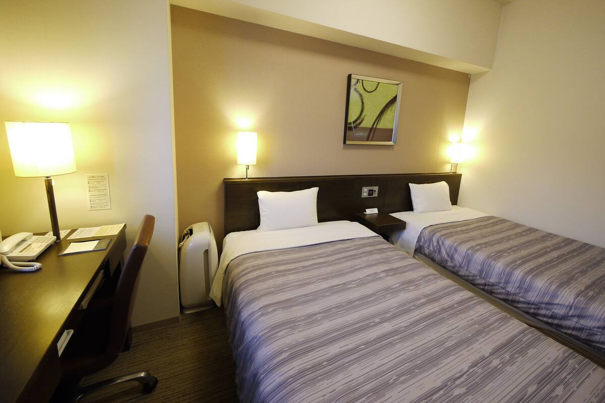 A hotel room with two beds, a desk with a telephone, and a chair.