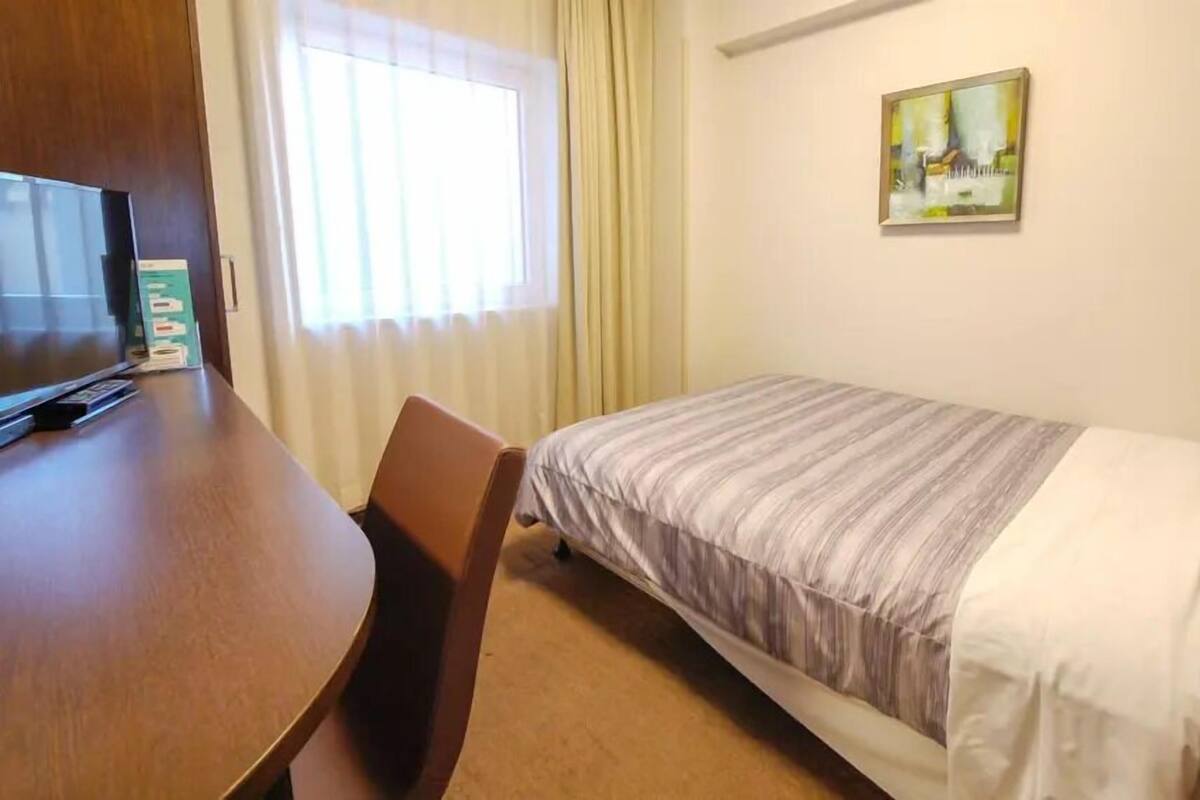 A hotel room with a bed, a desk, a chair, a television, and a window with curtains.