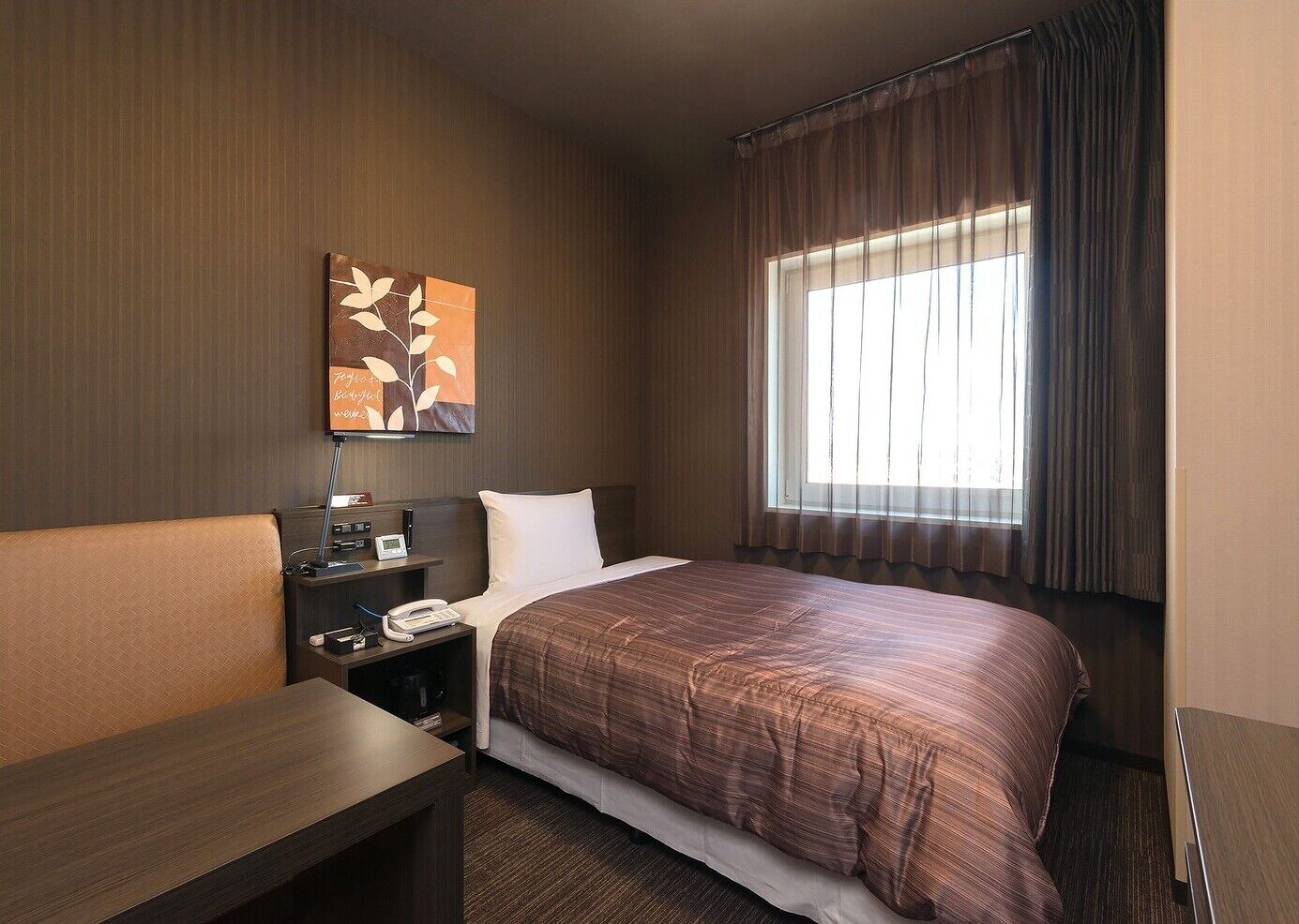 Een hotelkamer met een bed, nachtkastje, lamp, telefoon en een schilderij aan de muur.