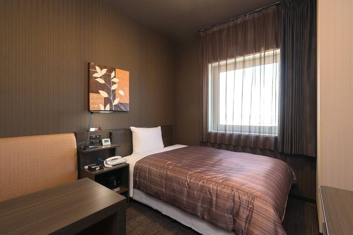 A hotel room with a bed, bedside table, lamp, phone, and a painting on the wall.