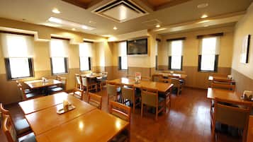 Un restaurante con mesas y sillas de madera, ventanas amplias y un televisor de pantalla plana en la pared.