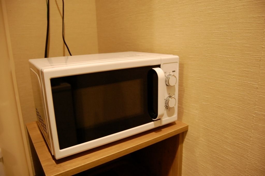 A white microwave on a wooden shelf in a room with beige walls.