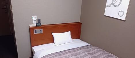 Habitación de hotel con cabecera de madera, almohada blanca, colcha a rayas, un reloj y una obra de arte colgada en la pared.