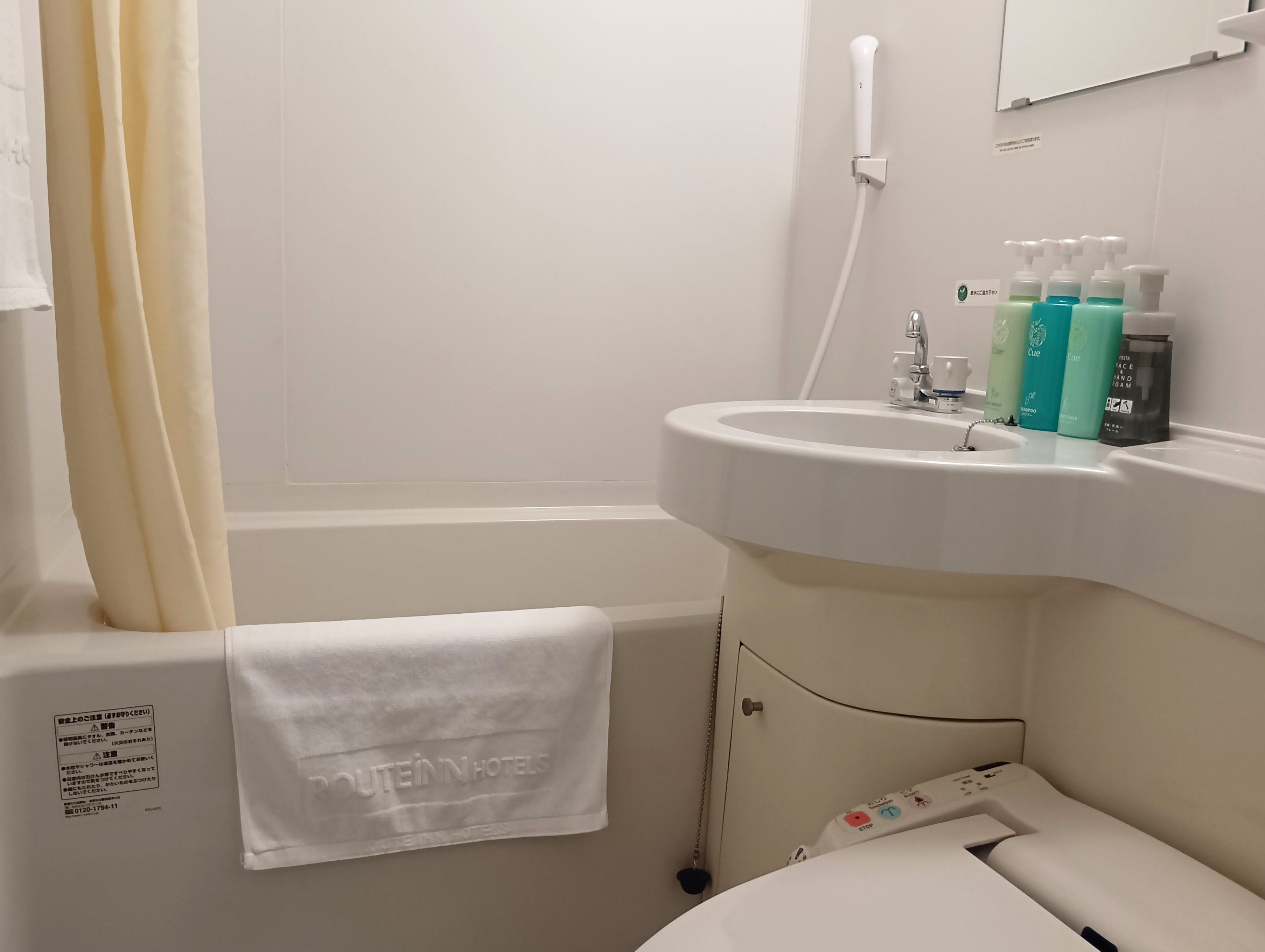 Een badkamer met een bad, een wastafel met toiletartikelen en een handdoek aan de muur.