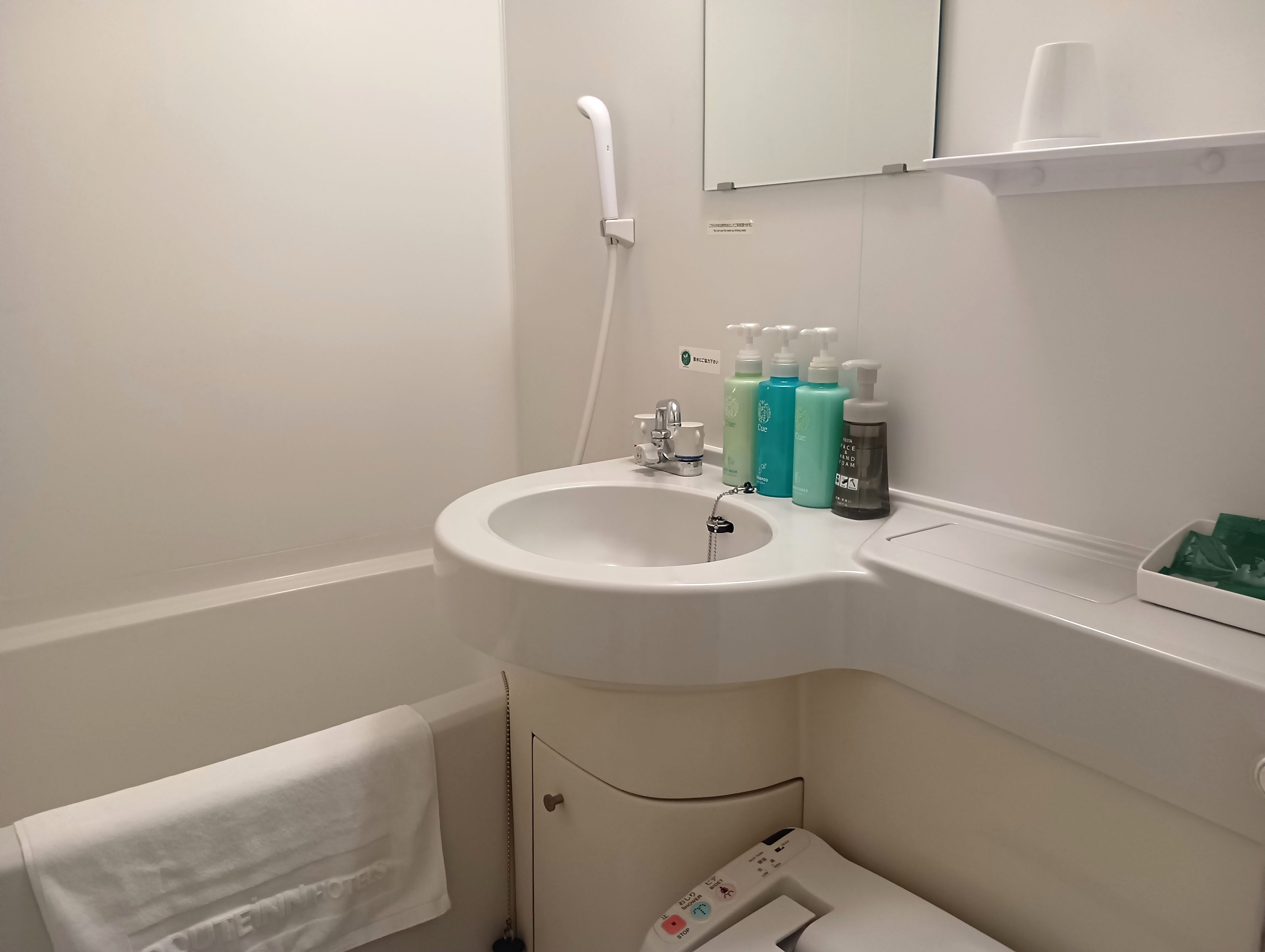 Un baño con un lavamanos blanco, un espejo y un inodoro. Hay artículos de aseo en la encimera del lavamanos.
