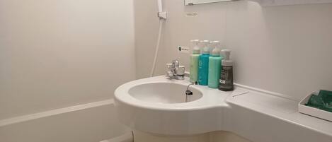 Un baño con un lavamanos blanco, un espejo y un inodoro. Hay artículos de aseo en la encimera del lavamanos.