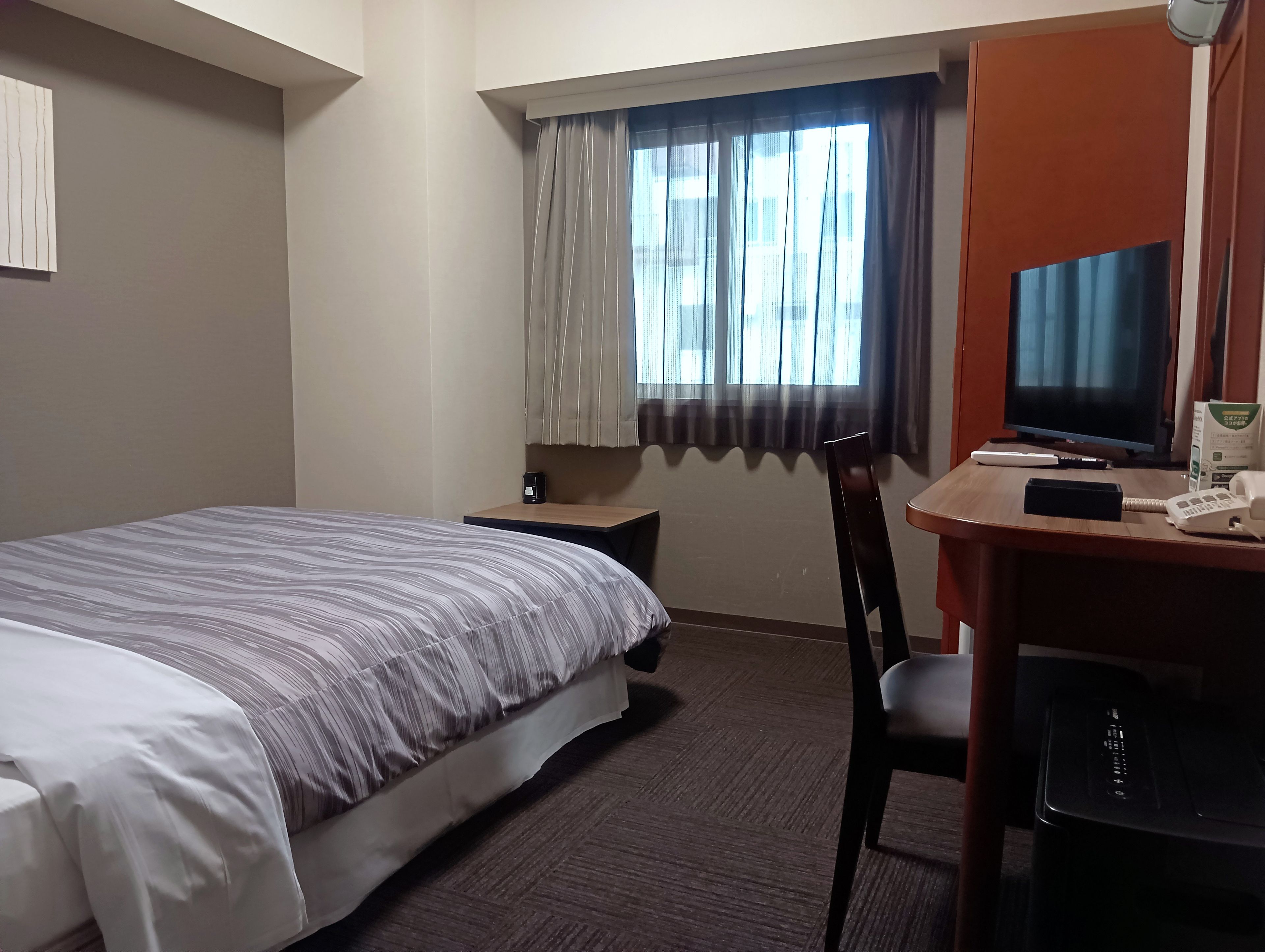 Une chambre d’hôtel comprenant un lit, un bureau avec une télévision, une chaise et une petite table avec une machine à café.