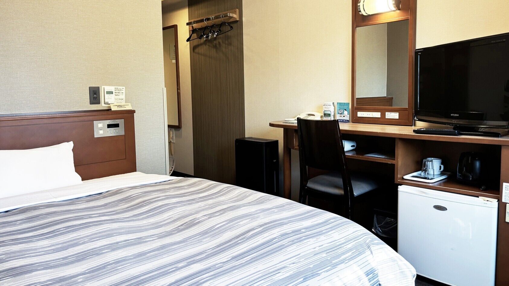 A hotel room with a bed, a desk with a chair, a television, a coffee maker, and a mini-fridge.
