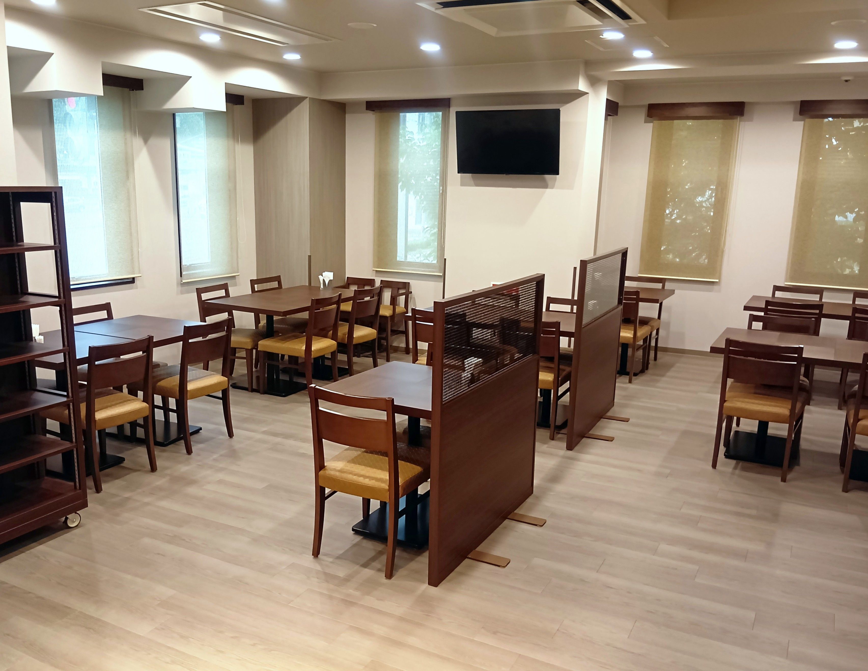 A conference room with multiple tables and chairs, a large screen, and windows with blinds.