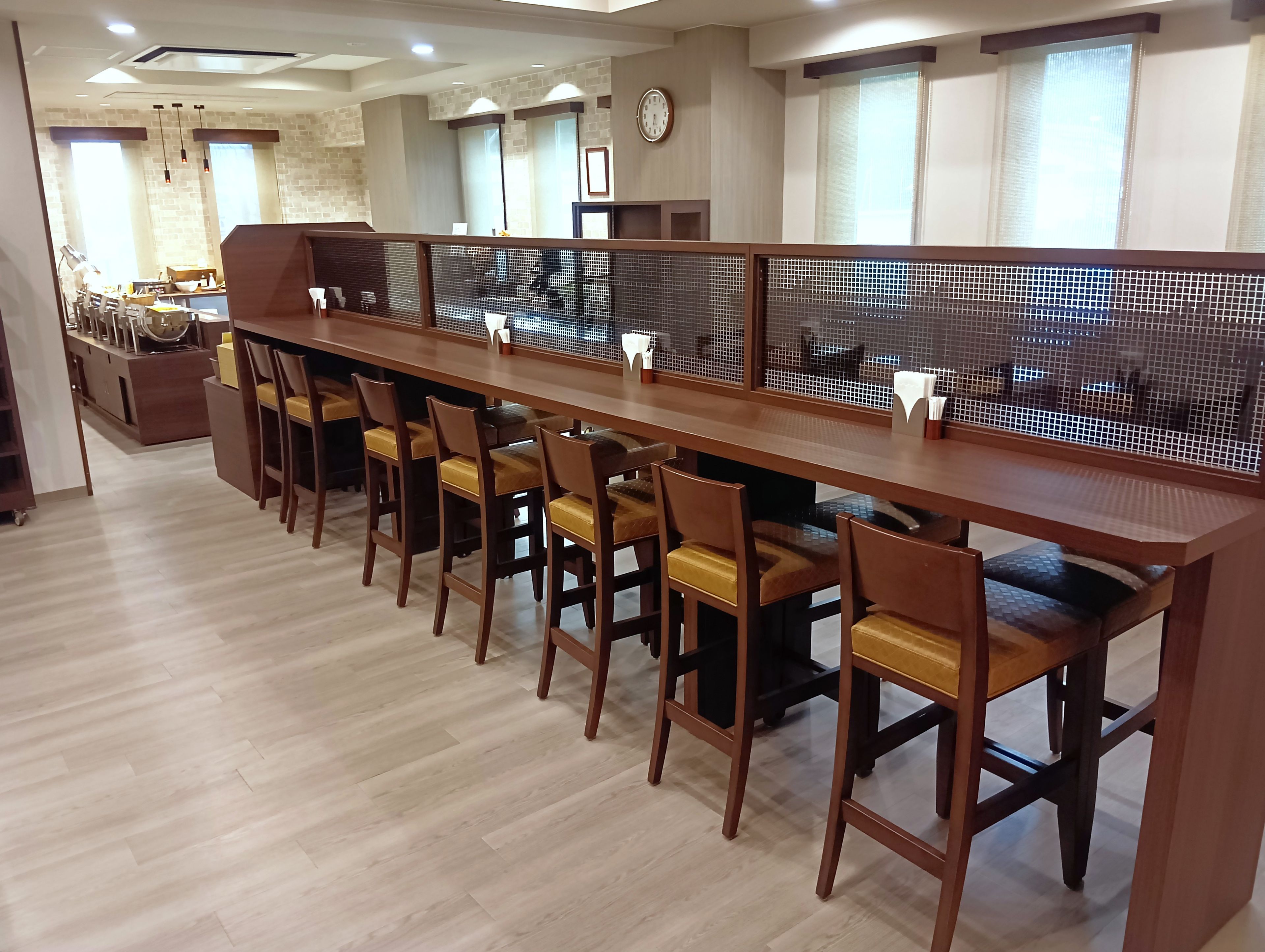 A long dining table with chairs, partition screens, and a clock on the wall.