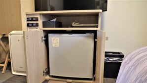 A compact refrigerator in a hotel room, a small trash bin, and a bed with a striped blanket. - Hotel Route Inn Abashiri Ekimae (Abashiri)
