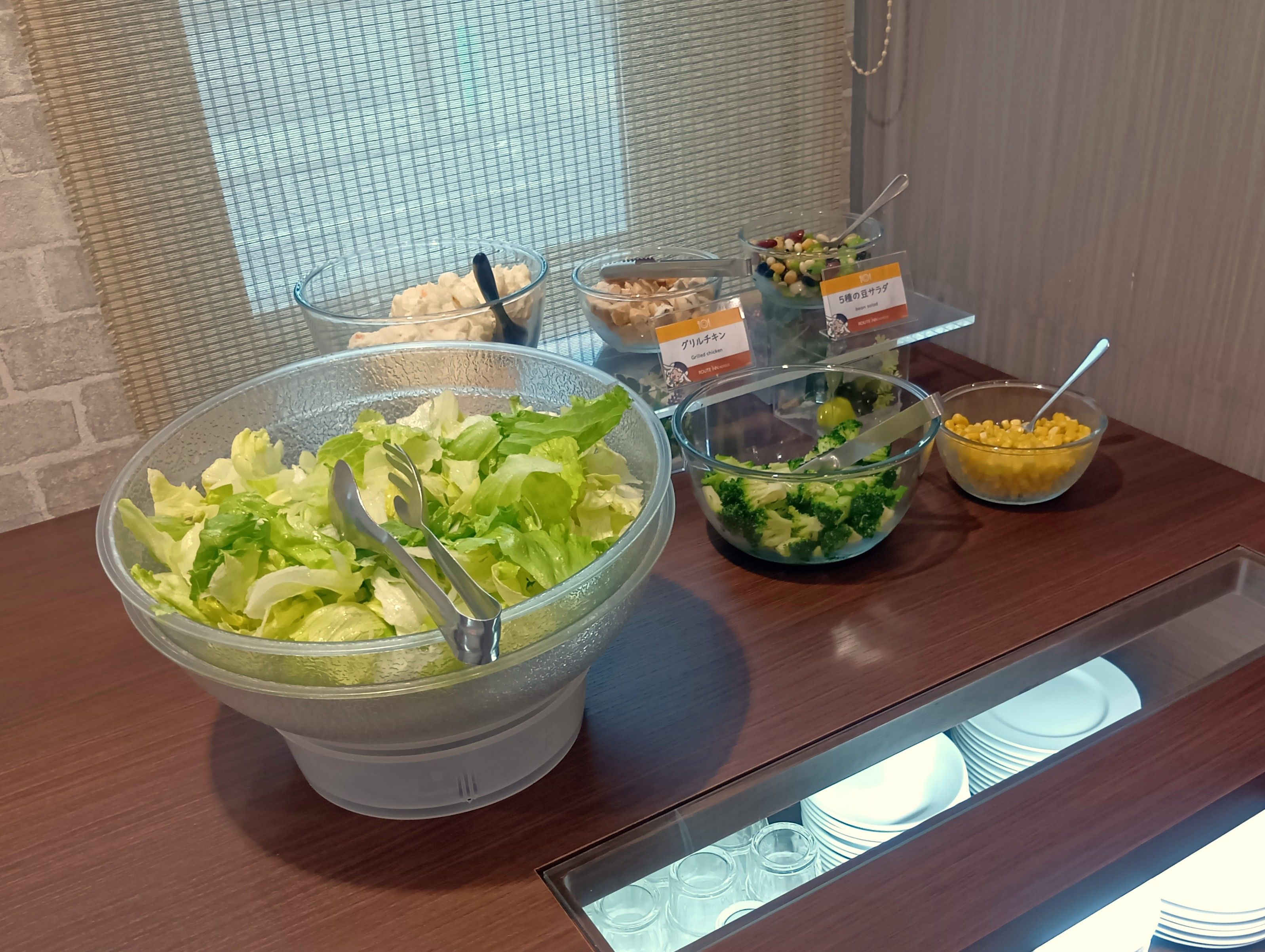 A buffet table with various food options including a large bowl of salad, a bowl of broccoli, and a bowl of corn.