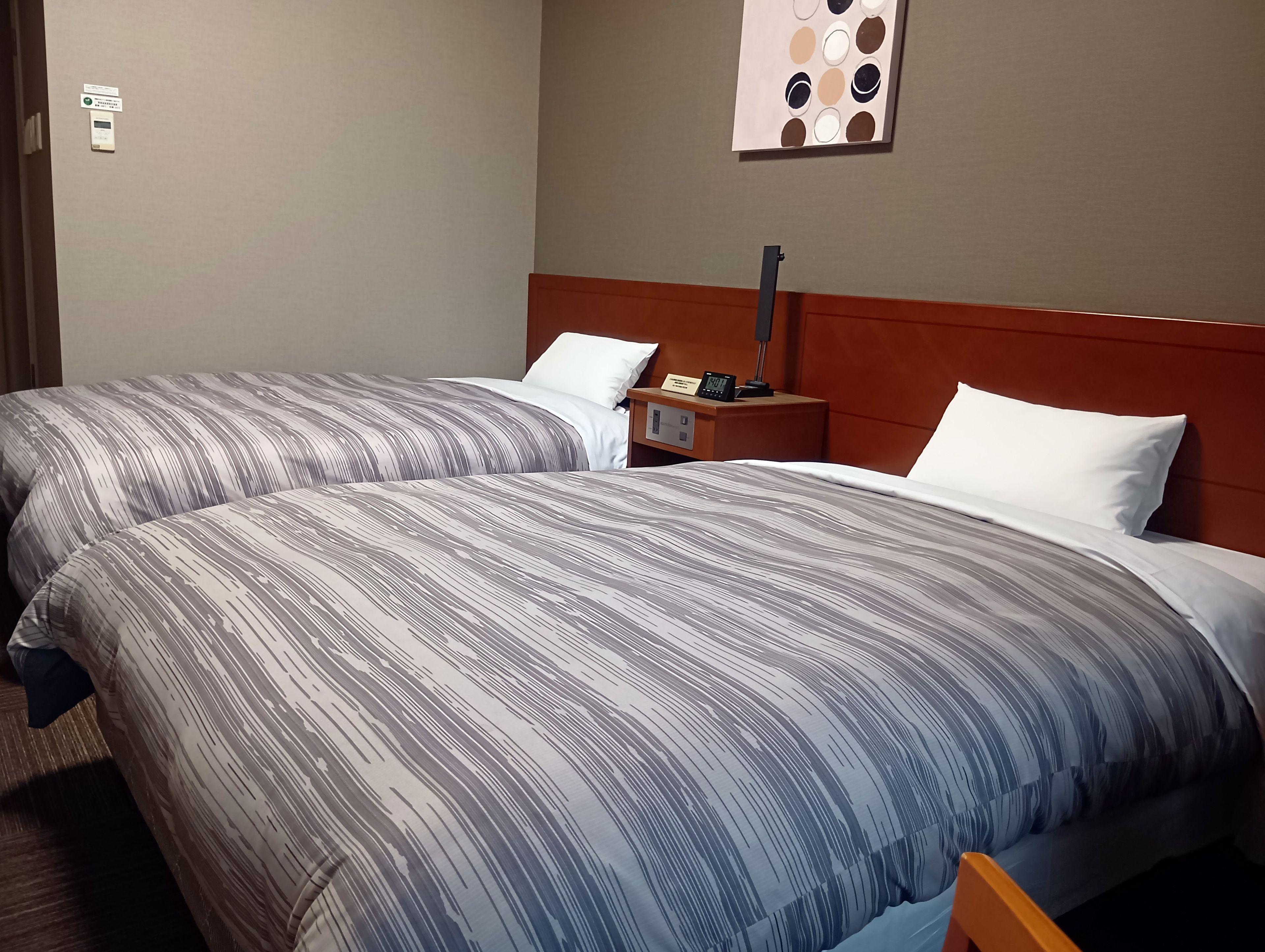 Habitación de hotel con dos camas, una mesita de noche con un teléfono y una lámpara, y una obra de arte colgada en la pared.