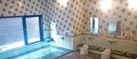 A bathroom with a stone floor, tiled walls, a glass-enclosed shower, and a sink with a mirror.