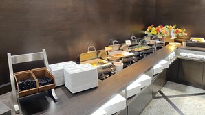 En buffé med serveringsbord i rostfritt stål, ett urval av matbehållare och en dekorativ blomsterarrangemang.
