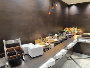 Montaje de buffet con mostradores de acero inoxidable, diferentes recipientes de comida y una decoración floral.