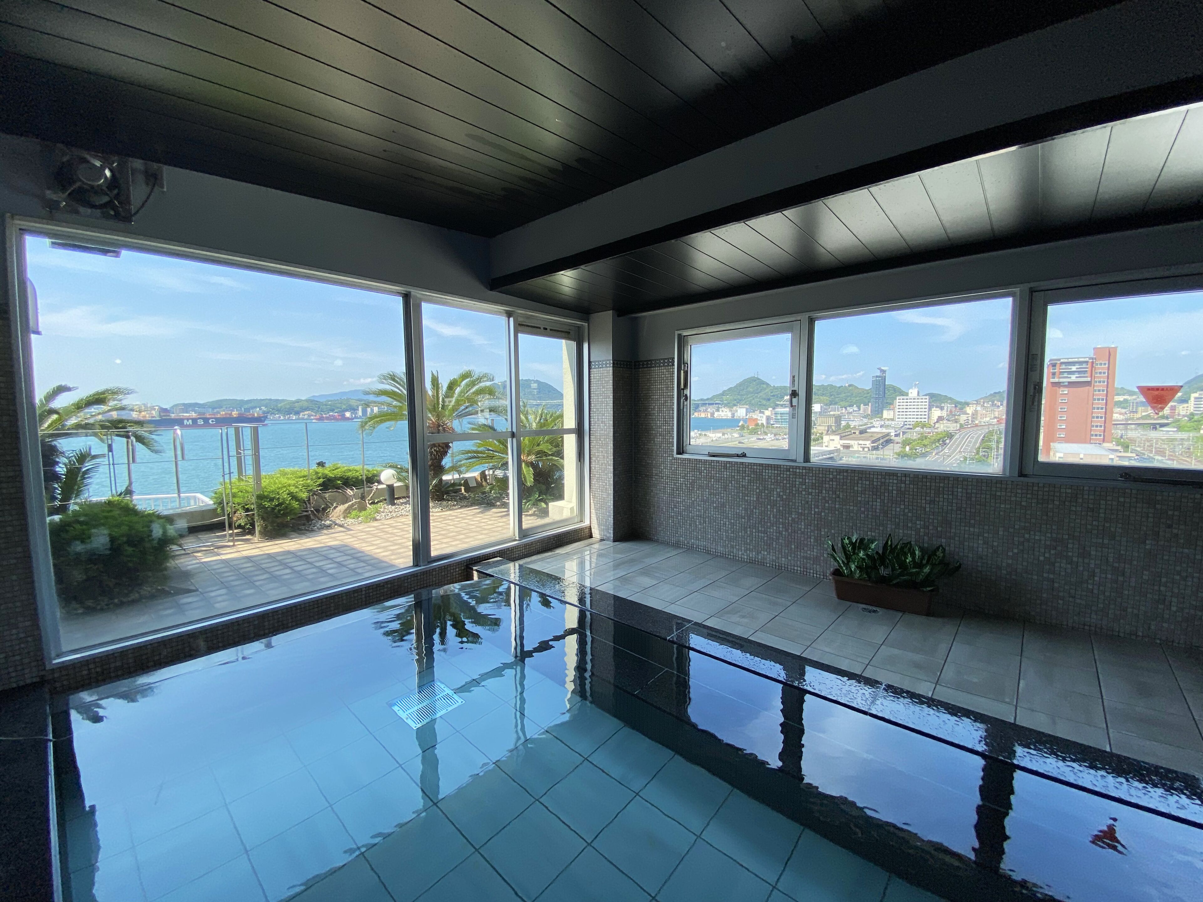 A modern indoor swimming pool with large windows offering views of a coastal cityscape.