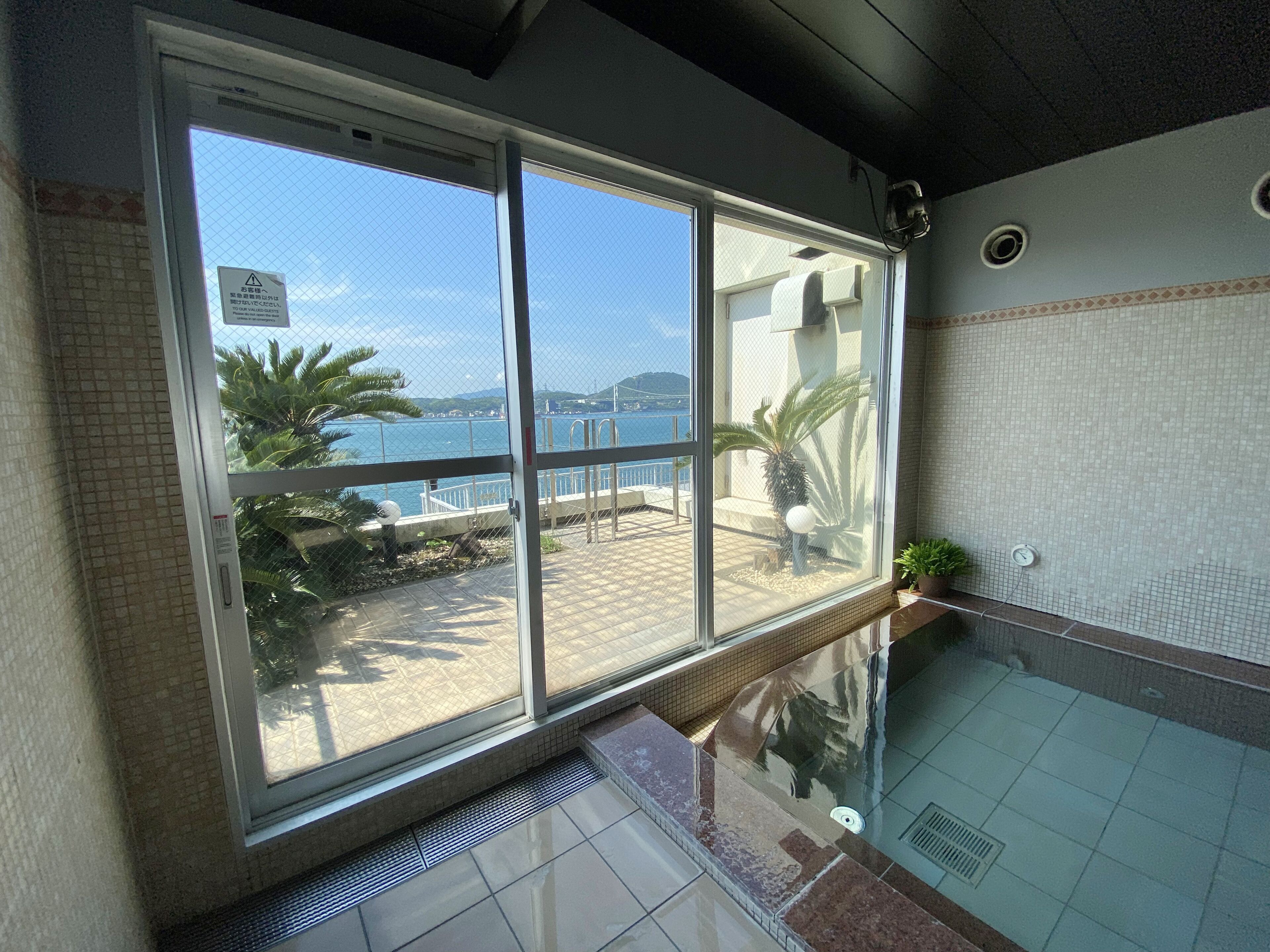Una stanza con una grande finestra che si affaccia su un balcone con vista sul mare e sulle montagne.