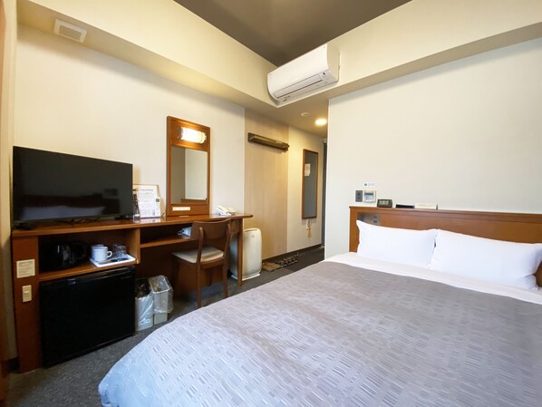 A hotel room with a bed, a desk with a television, a chair, a mirror, and an air conditioning unit. - Hotel Route-Inn Mojikou (Kitakyushu)
