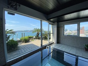 A modern interior with large windows, a glass pool, and a view of the sea and cityscape. - Hotel Route-Inn Mojikou (Kitakyushu)