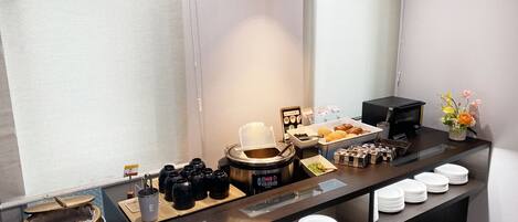 A buffet setup with various food items, a coffee machine, and a small flower arrangement.