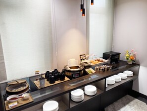 A buffet setup with various food items, a coffee machine, and a small flower arrangement. - Hotel Route-Inn Mojikou (Kitakyushu)