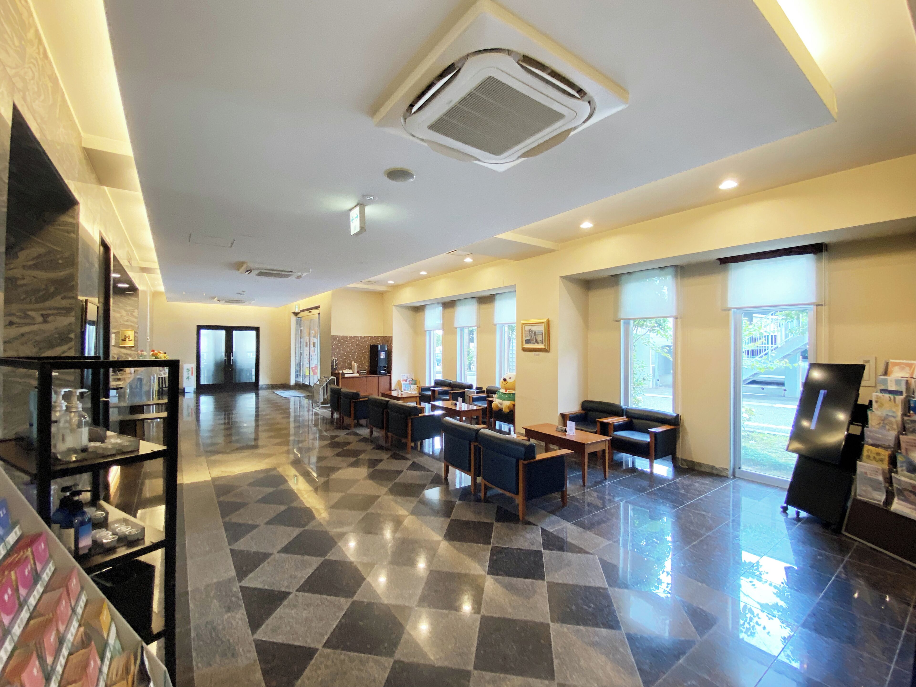 A hotel lobby with a checkered floor, seating areas, a reception desk, and large windows.