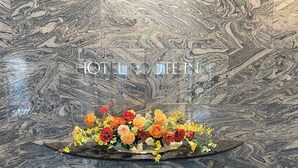 En vägg av marmor med texten ”HOTEL ROUTE INN” och en blomsterdekoration på en mörk yta.