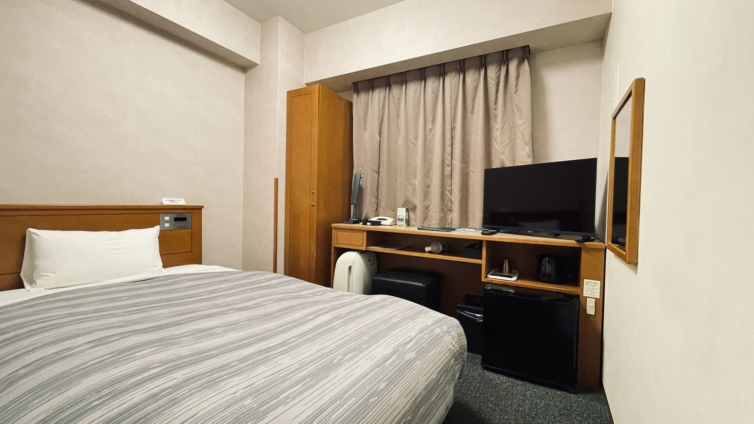 Une chambre d’hôtel comprenant un lit, un bureau avec une télévision, un petit réfrigérateur et une armoire.