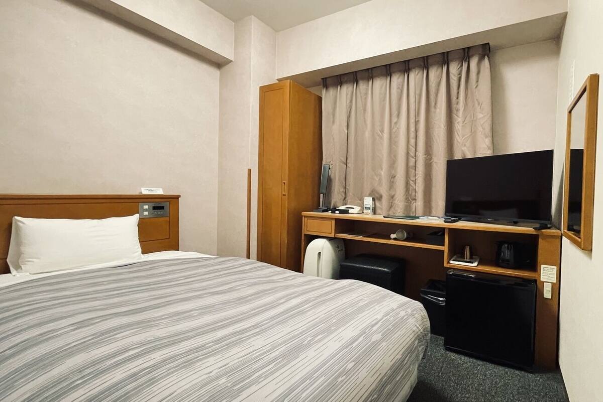 Une chambre d’hôtel comprenant un lit, un bureau avec une télévision, un petit réfrigérateur et une armoire.