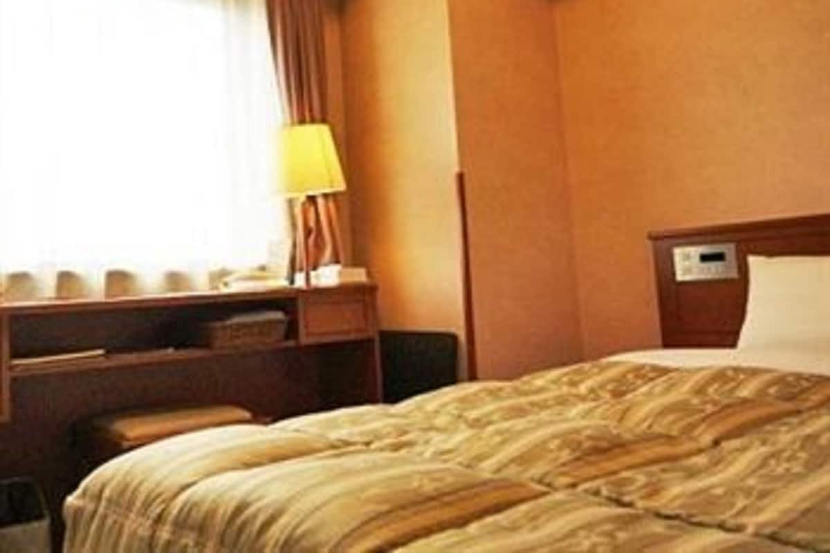 Une chambre d’hôtel avec un lit, un bureau doté d’une lampe et une fenêtre avec des rideaux.