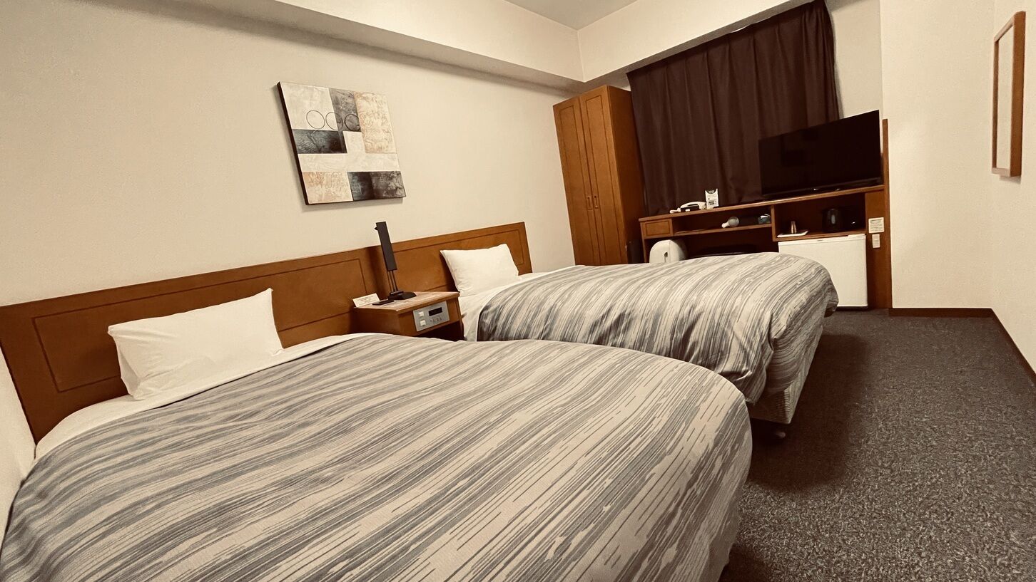 Une chambre d’hôtel avec deux lits, un téléviseur à écran plat, un bureau et une grande fenêtre avec des rideaux.