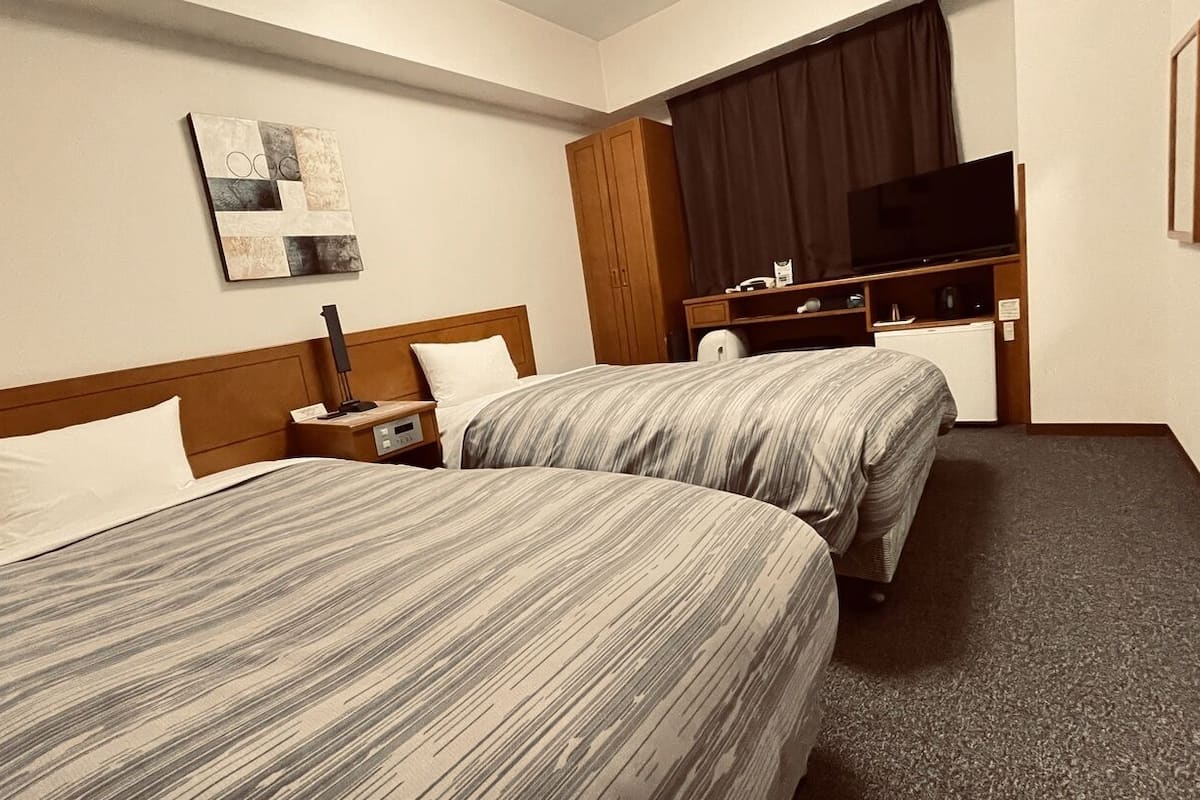 Une chambre d’hôtel avec deux lits, un téléviseur à écran plat, un bureau et une grande fenêtre avec des rideaux.