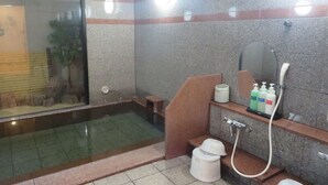 Uma casa de banho com chuveiro separado por vidro, sanita e lavatório com artigos de higiene pessoal.