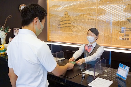 A reception desk with a glass partition, a framed artwork of a pagoda, and a small table with a calendar and a phone.