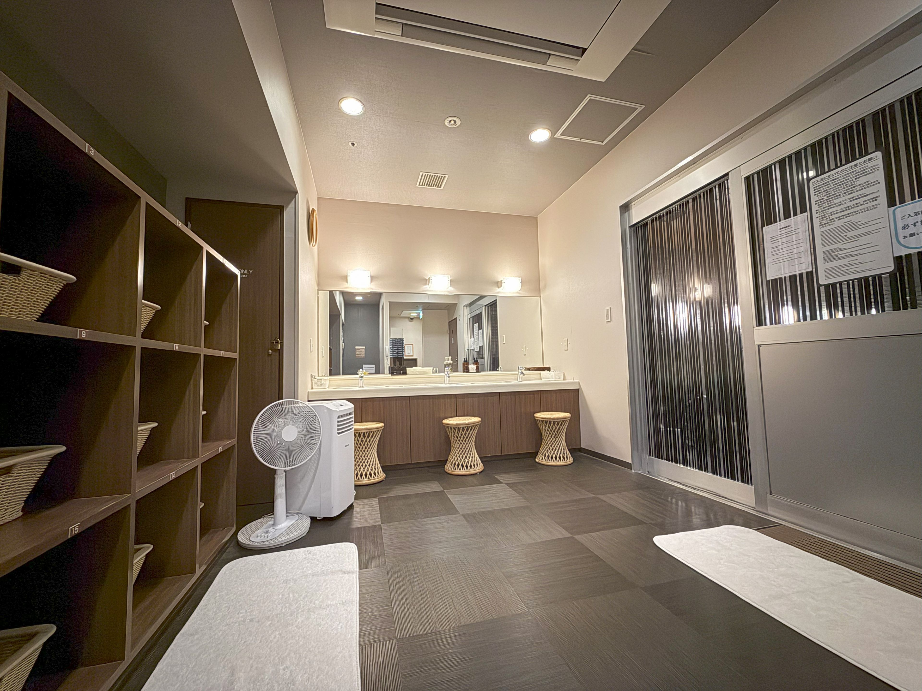 A hotel bathroom with a large mirror, a sink, and a fan.