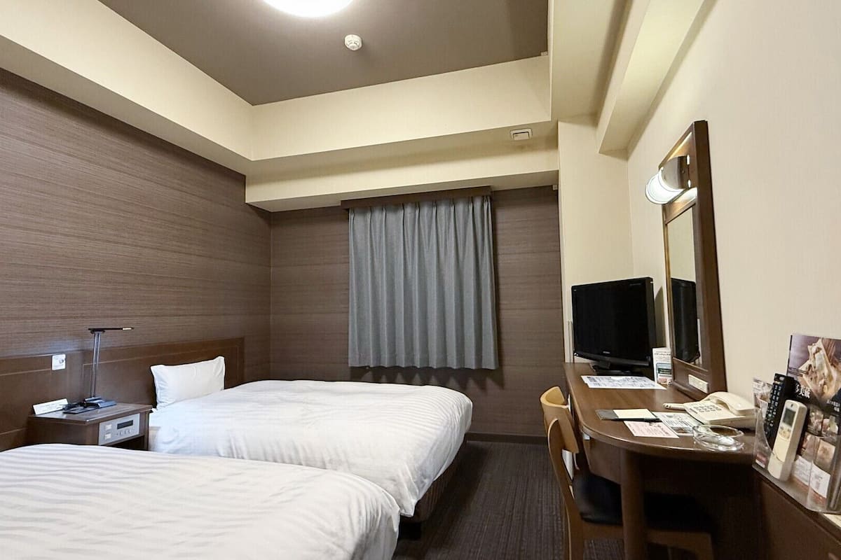 A hotel room with two beds, a desk with a computer, a TV, and a mirror.