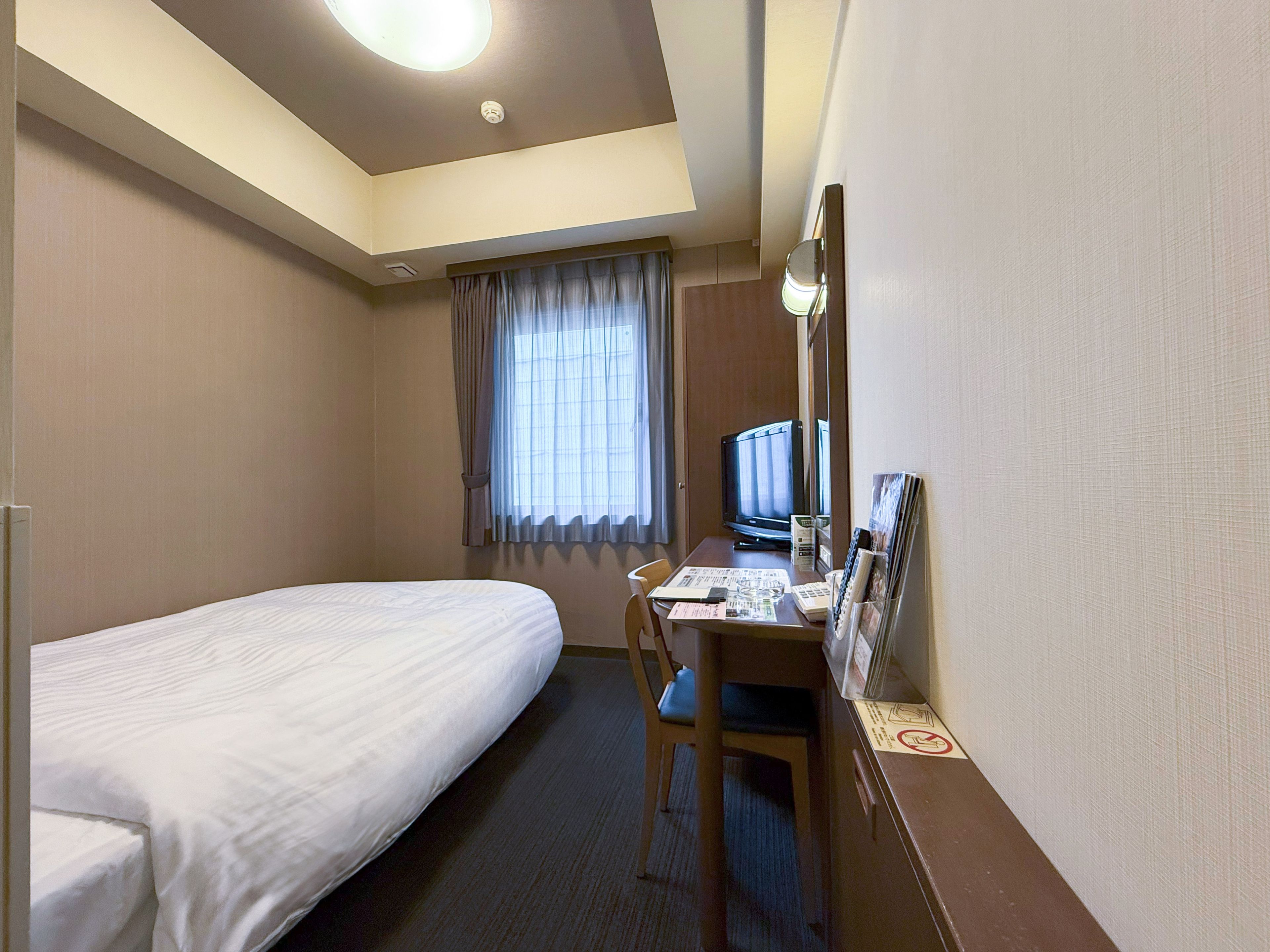 Una habitación de hotel con una cama individual, un escritorio con computadora y televisión.