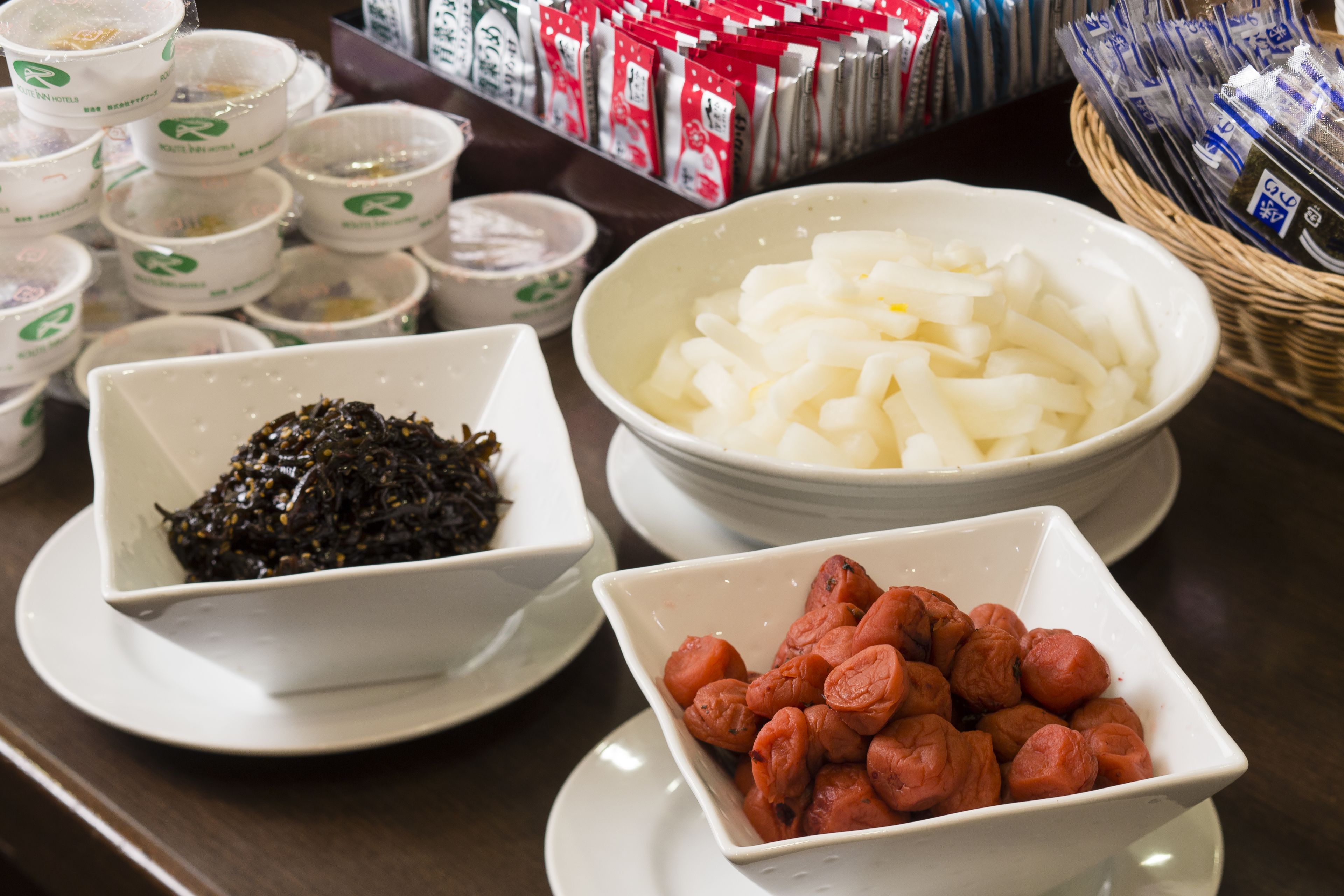 A table with bowls of food, including seaweed, white noodles, and sausages.