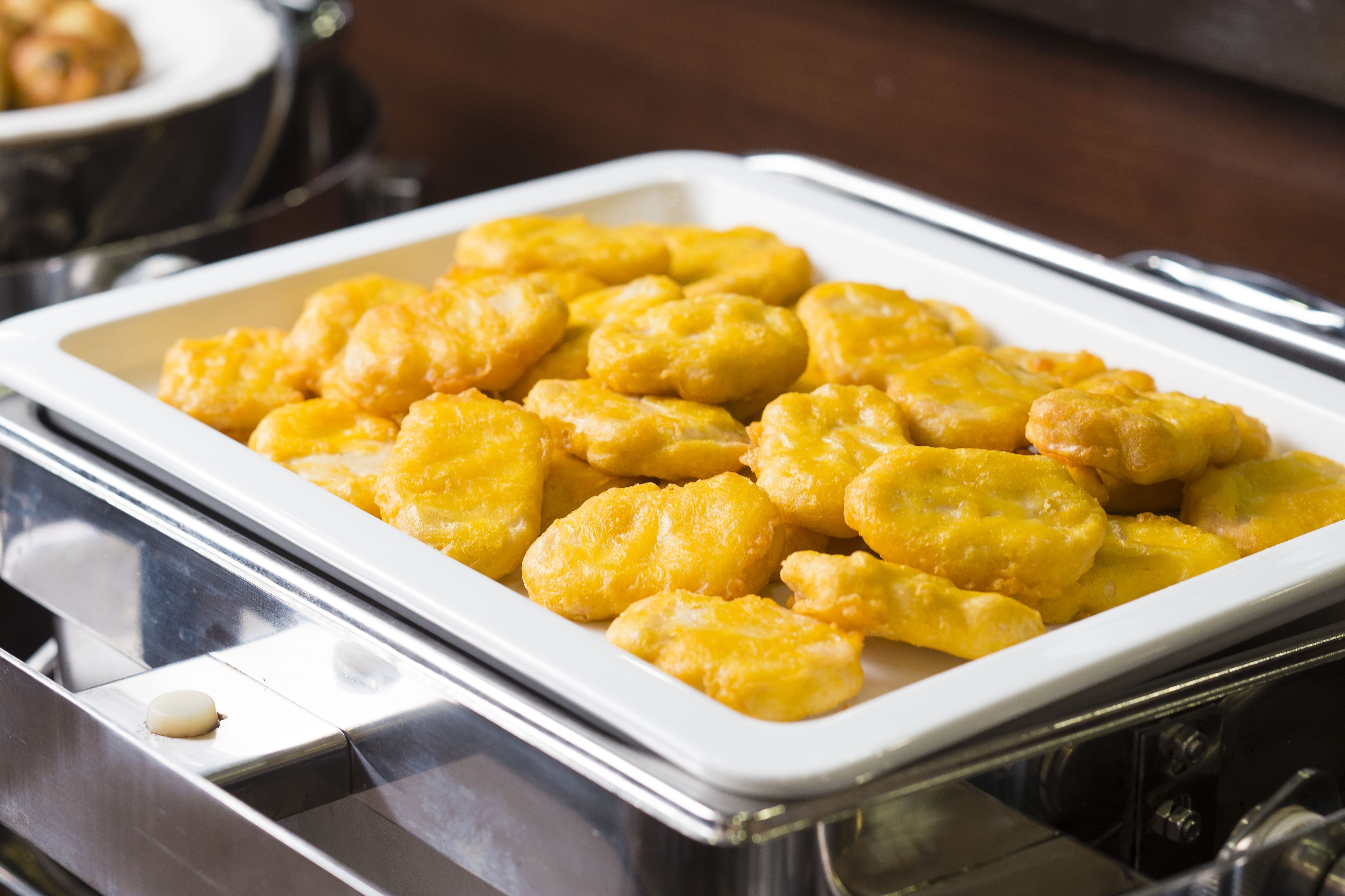 A tray of golden-brown fried food items, likely fritters, in a white rectangular dish.