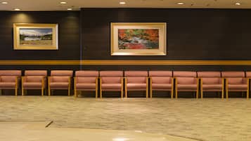 A lobby with a row of pink cushioned seating, a patterned carpet, and two framed landscape paintings on the wall.