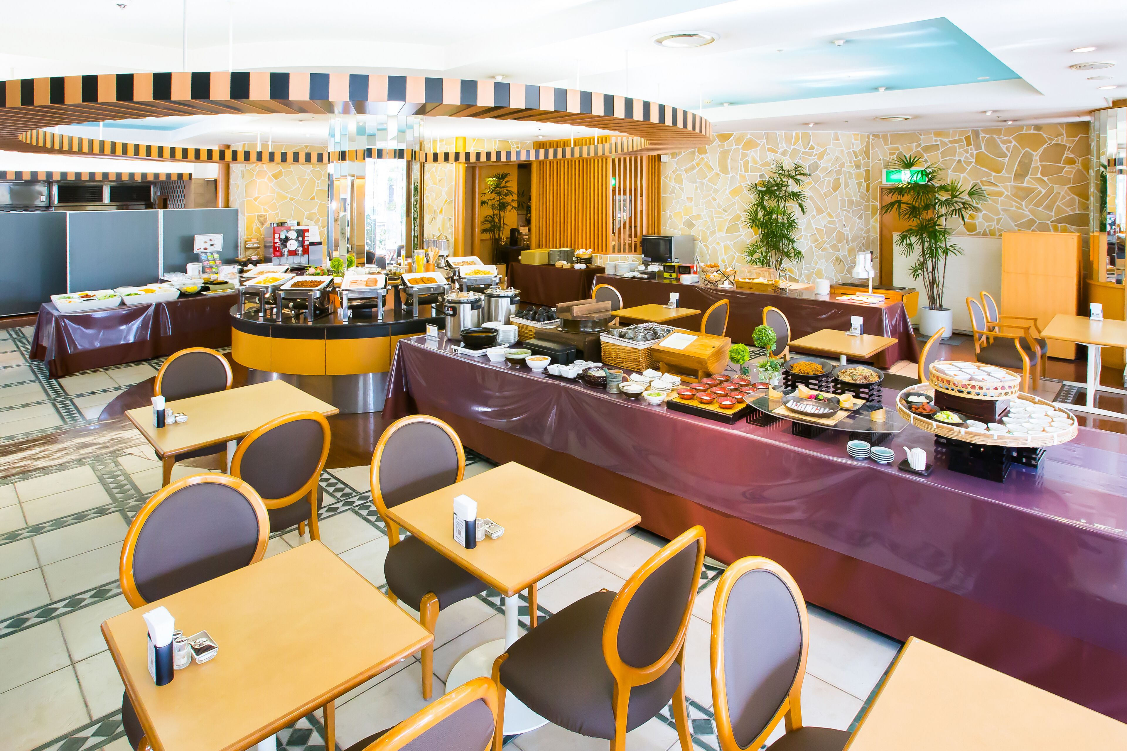 Een restaurant in buffetstijl met meerdere eettafels en stoelen, diverse thematafels en een achtergrond van een stenen muur.