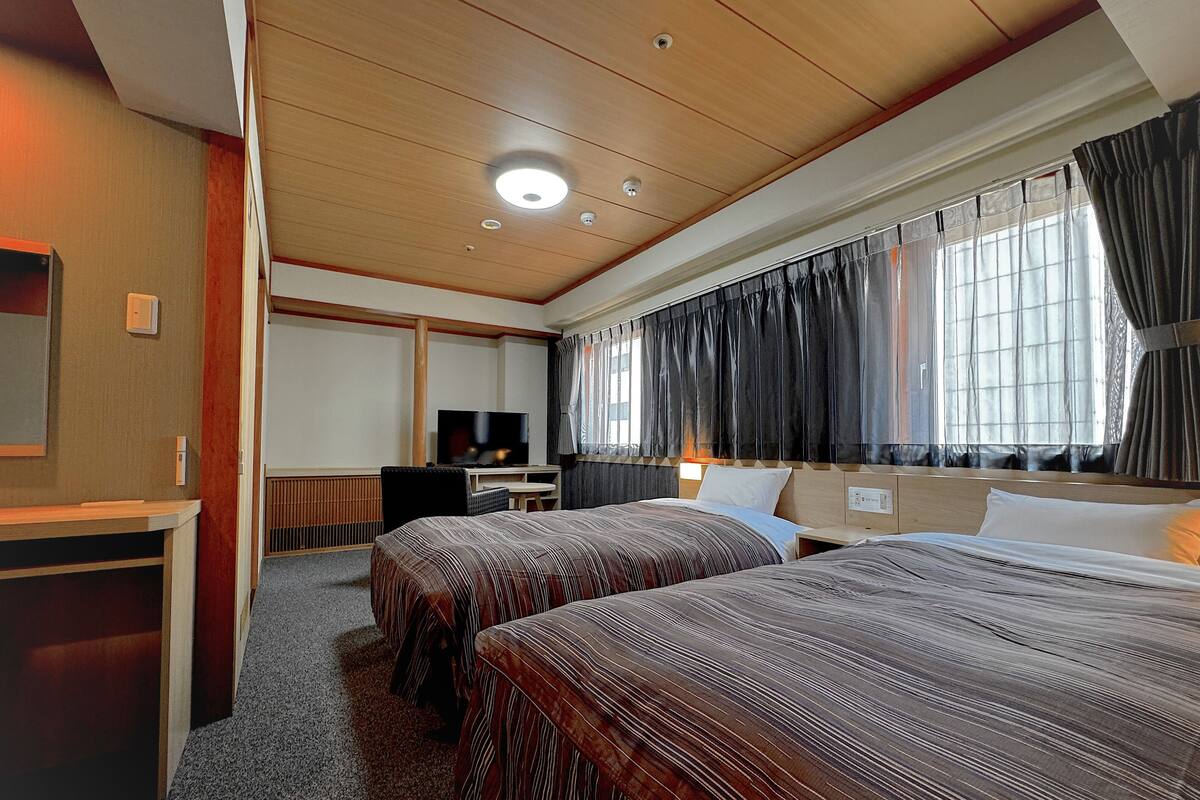 Una habitació d'hotel amb dos llits, una taula de treball, televisió i una finestra amb cortines.