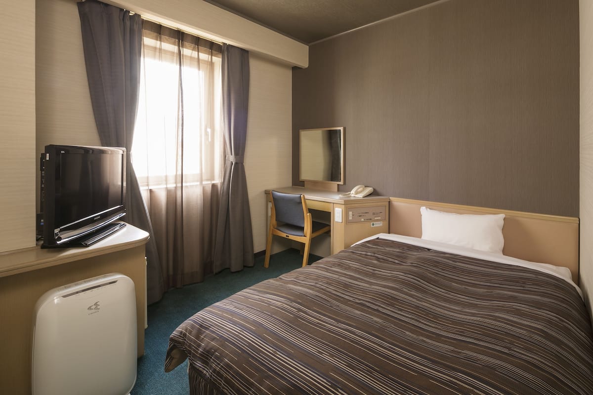 Habitació d'hotel amb llit, escriptori, cadira, televisió i nevera petita.
