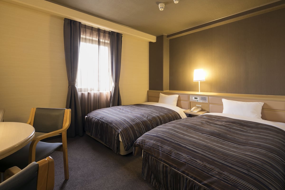 Habitació d'hotel amb dos llits, un escriptori, una cadira i una làmpada.