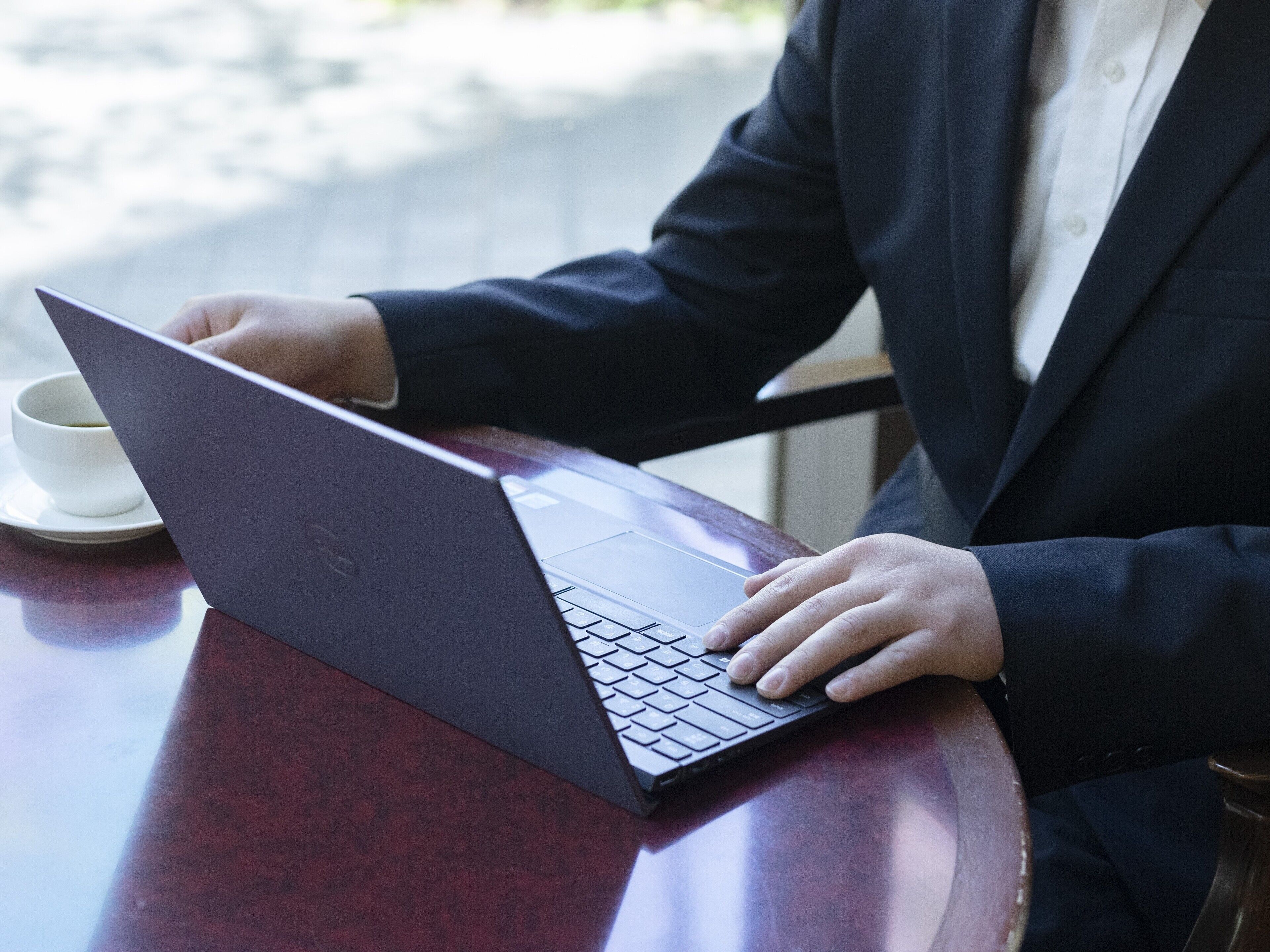 Une personne utilise un ordinateur portable sur une table en bois, avec une tasse blanche à proximité.