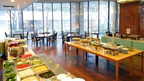 Un buffet est installé dans une pièce spacieuse dotée de grandes fenêtres, avec différents stands de nourriture, des tables et des chaises disposées de manière harmonieuse.