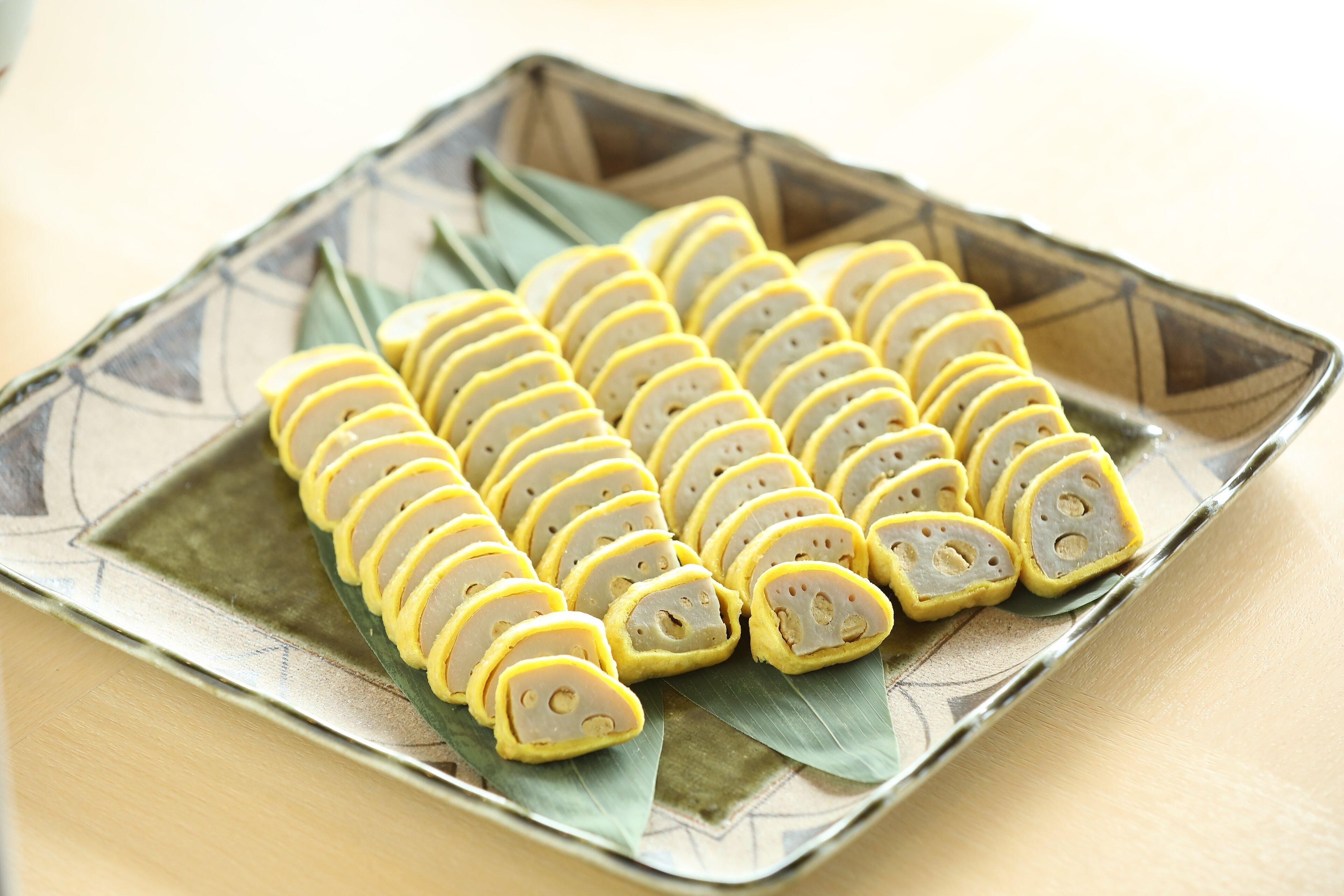 A square plate with neatly arranged yellow and white slices of food, possibly a type of cake or pastry, on a decorative ceramic plate with a geometric pattern.